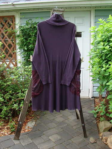 A medium weight cotton thermal dress in cherry plum with a turtleneck, side pockets, and a slight varying hemline. Features include exterior stitchery, a longer rounded A-line shape, and lettuce edges. Size 1.