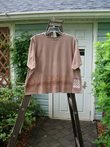 2000 Short Sleeved Crop Tee with Floral Fence Border in Coralline. Mid-weight organic cotton shirt on a wooden ladder. Close-up of wood post and plant.