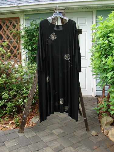 A 1995 Acetate Lycra Celebration Dress in Onyx, size 2, on a wooden rack. Sweeping lettuce-edged varying hemline, A-line flare, thin rounded neckline.