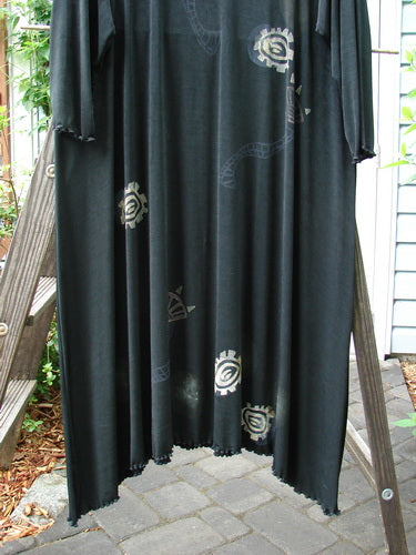 1995 Acetate Lycra Celebration Dress with Celtic Turn design. A black dress on a wooden stand. Lettuce-edged hemline, A-line flare, and rounded neckline. Size 2.