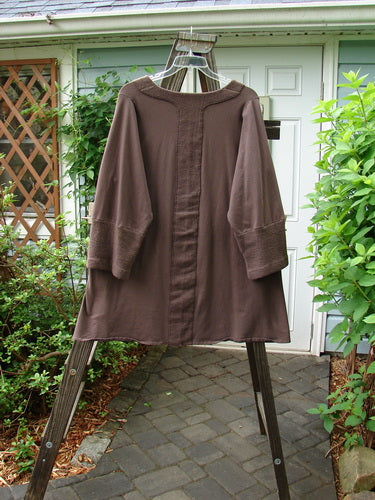 Image alt text: Barclay Cotton Lycra Celtic Moss Single Pocket Tunic Top in Mocha, featuring a brown robe on a swinger, long brown robe on a rack, close-up of a plant, close-up of a lattice, wooden post with a screw, close-up of a lamp, close-up of a bush, stone walkway with a brown cloth.