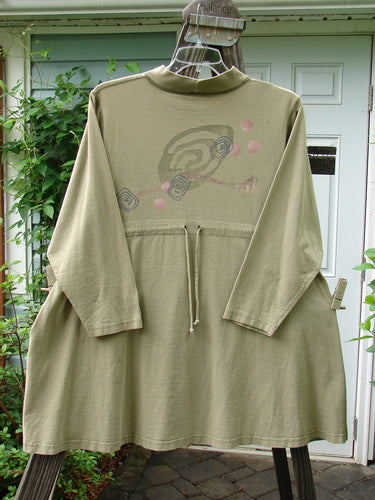 A long green shirt on a swinger, 1996 Ramble Dress Follow Path Bottlecap Size 1, made from Organic Cotton. Features include a ribbed mock T neck, oversized front pocket, adjustable draw, and exterior stitching. Bust 48, Waist 52, Hips 56, Sweep 80, Length 36.