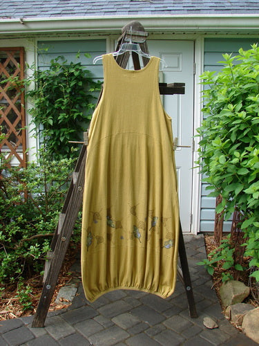 A 2000 Cotton Hemp Libby Jumper in Fall Leaf Gold, Size 1. A dress on a rack with a downward scooped waistline, bubbled shape, and elastic hemline. Features include 2 side pockets and a bottom accented seam.