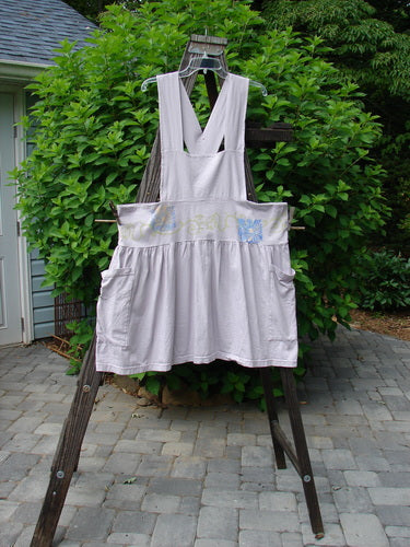 Image alt text: "Vintage 1995 lavender overall jumper with daisy curl design, featuring a white apron on a wooden rack"