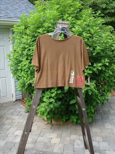 1992 Short Sleeved Crop Tee with Flower Power design on brown shirt, displayed on wooden stand. Vintage collectible from BlueFishFinder.