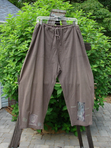 1994 Wanderer's Pant Spirit Woman Humus Size 1: A pair of pants on a clothes rack. Medium weight cotton jersey. Drawstring waistline, side entry front pockets, crop length, widening rounded hip, and Spirit Woman theme paint.