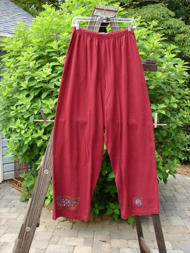 1997 Simple Pant Love Dove Regalia Size 1: A pair of red pants on a clothes rack, featuring a full elastic waistband, deep side pockets, and a slightly straighter fall. Made from organic cotton, this vintage piece from Blue Fish Clothing's Spring Collection is in perfect condition.