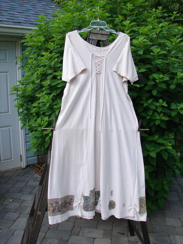 A white dress on a clothes rack, featuring a sweeping A-lined shape, dual cord lacings on the front and back upper bodice, and a super flared hemline. This 1994 Loop Dress from the Magic Garden Tea Dye collection is a unique and smaller piece from Blue Fish Clothing.