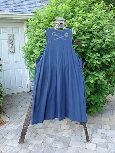 1996 State Fair Vest Directional Arrow Ridge Size 2: A blue dress on a wooden rack, with a single cloth covered oversized button, a double paneled hemline, and a wide A-line shape.