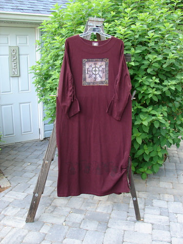 1999 Starlight Dress Deep Celtic Compass Deep Burgundy Size 2: A long-sleeved shirt on a rack with a red shirt featuring a picture and a black and white design.
