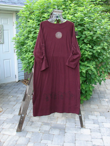 1999 Starlight Dress in Deep Burgundy, made from Mid Weight Organic Cotton. Features include a Rolled Double Layered Neckline, Sleeve Lacings, and a Straighter Longer Shape. Celtic Compass Theme Paint and Vertical Drawcord Accents. Bust 50, Waist 50, Hips 50, Length 54.