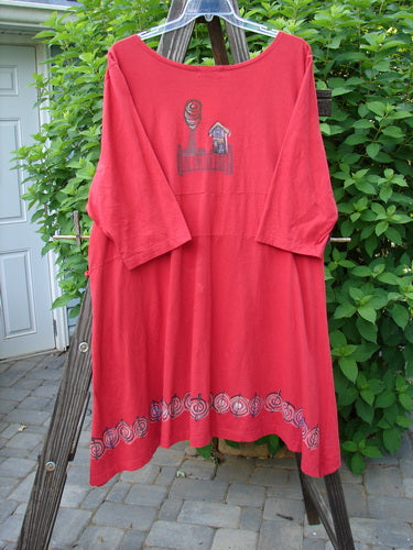 A red shirt with a picture on it, featuring a Super Deep V Shaped Neckline, Flat Tape Lacings, and a downward yoked Rear Drop Panel. The shirt has a slightly varying hemline, generous Leaf Theme Border Paint, and widening Three Quarter Length Sleeves. Size 2.