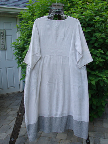 Barclay Linen Stripe Tulip Dress Unpainted Pebble Black Size 1: A white dress on a rack with a medium scoop neckline, three-quarter length sleeves, and a tulip bottom flare. Features oversized side interior pockets and contrasting pinstripe horizontal panel accents.