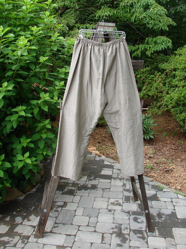 2000 Shaunting Silk Slant Drawcord Pant Cement Size 2: A pair of pants on a rack, made from Shaunting Silk. Rear elastic waistband with a drawcord front. Wider hips and lowers. Classic Transitions theme. Lengthier inseam and full length. Waist relaxed 26 to 56, waist extended 56, hips 56, inseam 26, length 40.