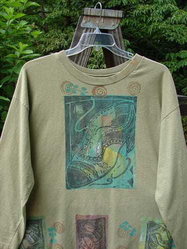 Image: A long sleeved shirt on a swinger. The shirt is from the 1992 Summer Collection in Rosemary. It is in perfect condition and made from medium weight cotton jersey. The shirt has a boxy longer shape, slightly shorter sleeves, and a thicker ribbed neckline. It features a vintage signature Blue Fish patch and abundant detailed fancy shoe theme paint. The measurements are as follows: Bust 50, Waist 50, and Length 30 inches.