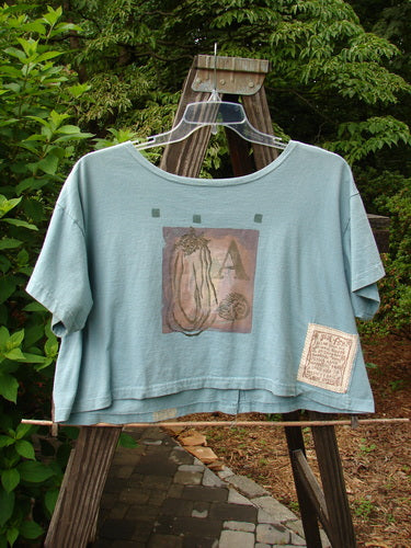 A 1994 Song Top Multi Letter "K" Ice Size 1. Image of a blue shirt on a swinger. Features a wide boxy shape, shallow neckline, vintage buttons, and a painted breast pocket.