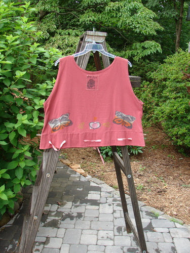 1992 Camisette Top Heart Sienna OSFA: A pink shirt with butterflies on it, hanging on a wooden rack.