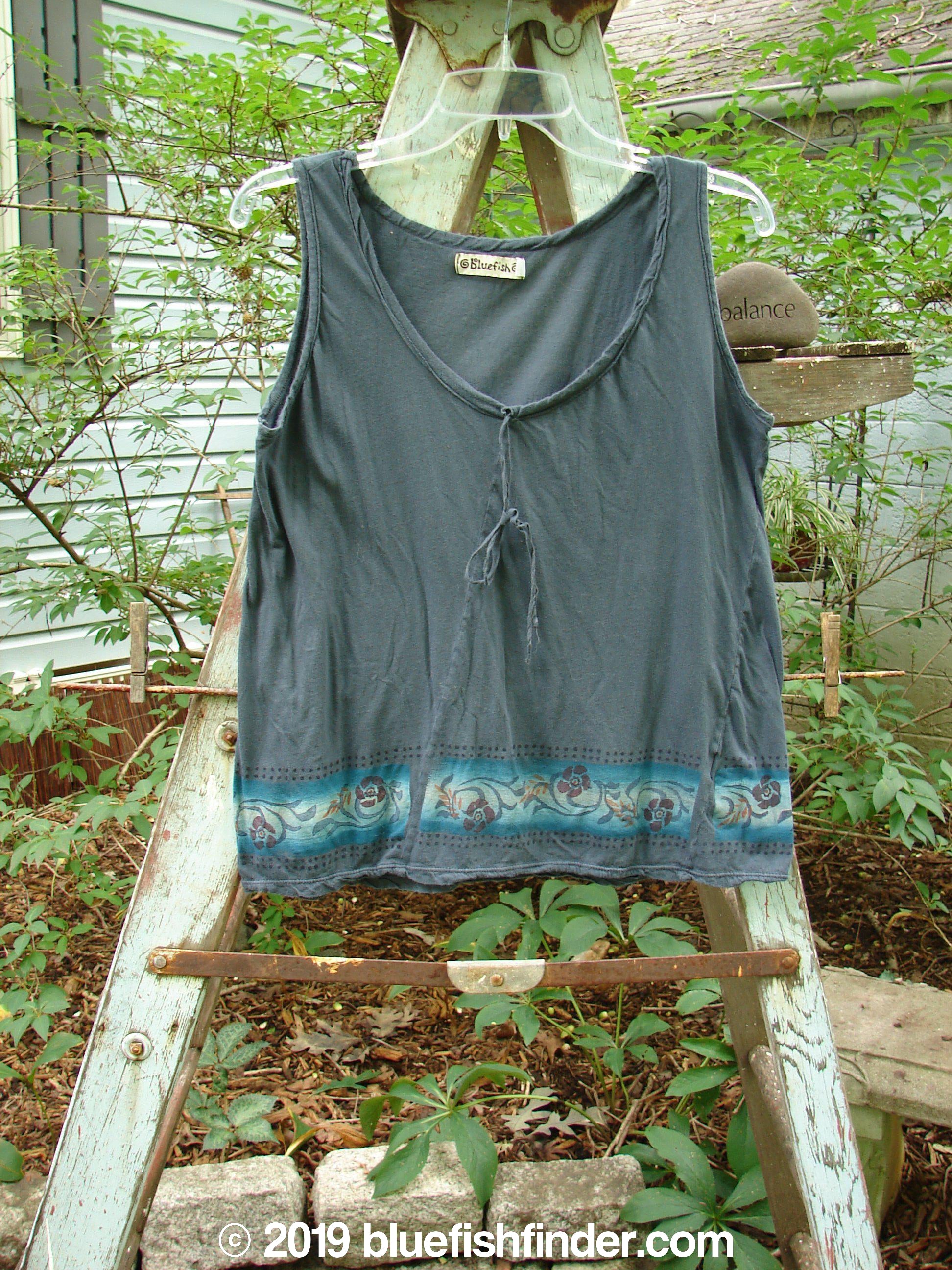 A grey tank top with a sweet front vertical neckline tie and gather, displayed on a wooden ladder.