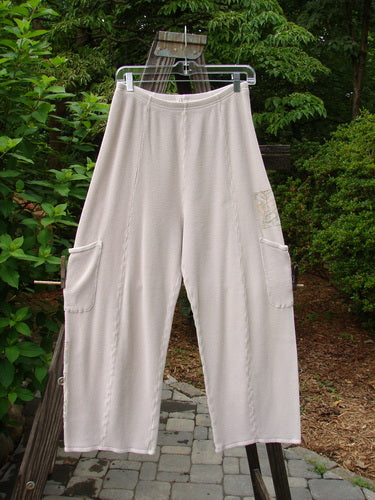 A pair of white pants on a clothes rack, featuring a full elastic waistline, vertical stitchery, generous hip measurements, and sweet painted garden patches. Size 1, Barclay Thermal Patched Pottery Pant in Pink Cloud.