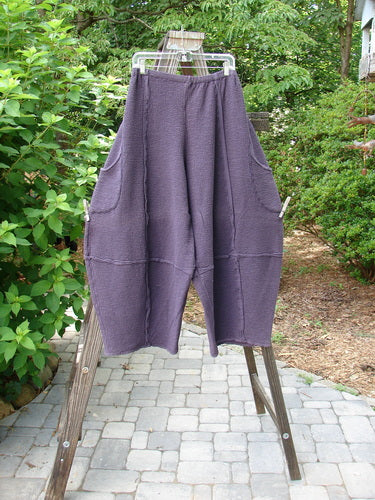 A pair of Barclay Crepe Sectional Pocket 4 Square Pants in Shadow, size 1, on a clothes rack. Unique bottom cut creates a 3D diamond shape from the knee down. Complete with generous hip pockets, elastic waistband, and textured fabric.