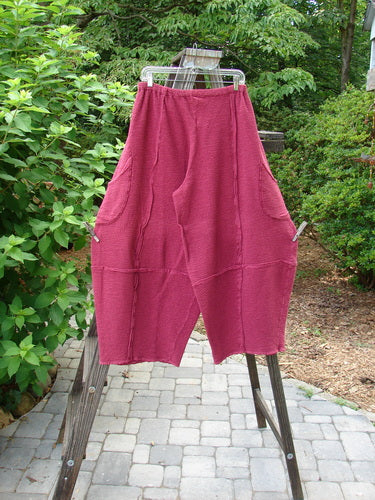 A pair of Barclay Crepe Sectional Pocket 4 Square Pants in Cranberry, made from Heavy Weight Cotton Crepe. Features a unique bottom cut that drapes into a 3D diamond shape from the knee down. Complete with exterior wrap-around hip pockets, elastic waistband, and rich texture. Size 1.