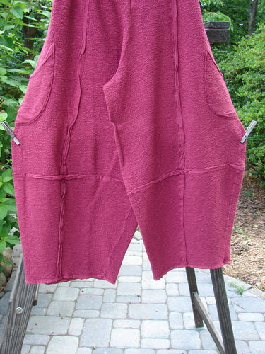 A pair of Barclay Crepe Sectional Pocket 4 Square Pants in Cranberry. Made from Heavy Weight Cotton Crepe, these pants feature a unique bottom cut that drapes into a 3D diamond shape from the knee down. Complete with exterior wrap-around hip pockets, a full elastic waistband, and rich texture. Size 1.