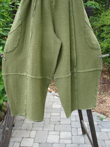A pair of Barclay Crepe Sectional Pocket 4 Square Pants in Olive, made from Heavy Weight Cotton Crepe. Features a unique bottom cut that drapes into a 3D diamond shape from the knee down. Complete with exterior wrap-around hip pockets, elastic waistband, and textured fabric. Size 1.
