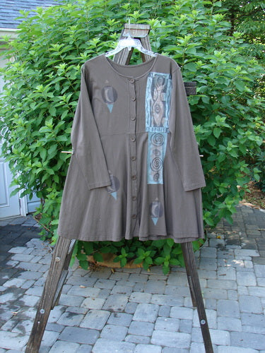 1994 Poppy Dress, collarless, figure eight woman, Humus, size 2. A brown shirt on a swinger, with a long brown coat on a wooden stand.
