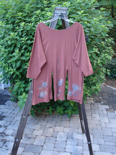 1994 Windmill Top Butterfly Clay Size 1: A red shirt on a wooden rack, with a long-sleeved pink shirt and a pink jumpsuit with a pattern on it nearby. A pair of pants on a rack can also be seen.
