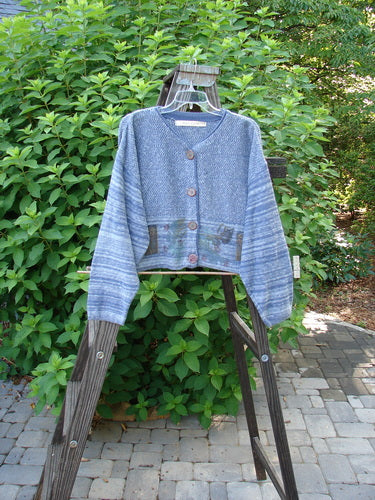 1994 Crop Cardigan Sweater Leaf Pod Haiku Blue OSFA: A sweater on a rack, featuring stoneware buttons, contrasting knits, and a leaf and pod theme.