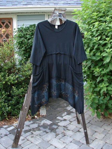 A black tunic dress with double pockets and a leaf garden theme paint. Three-quarter length sleeves and a varying hemline. Size 2.