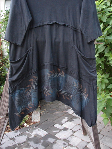 A black tunic dress with flutter seams, lettuce-edged sleeves, and a leaf garden theme paint. Features two drop front wrap-around pockets. Size 2.