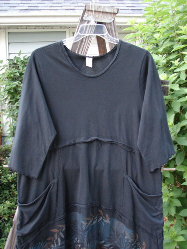 Barclay Reverse Stitch Double Pocket Tunic Dress: Black shirt on a swinger, featuring exterior flutter seams, lettuce-edged lower sleeves, and drop front wrap around pockets. Three-quarter length sleeves and a varying hemline. Made from mid-weight organic cotton.
