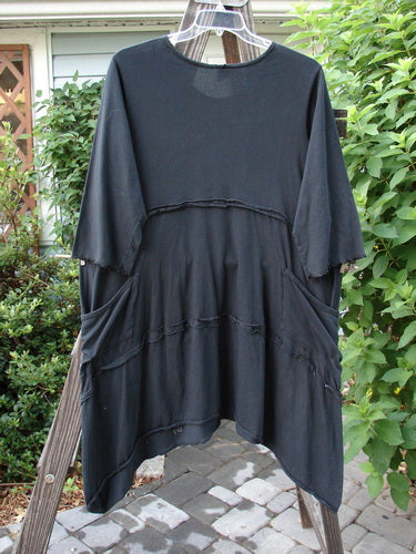 A black tunic dress with double pockets, flutter seams, and lettuce-edged sleeves. Made from mid-weight organic cotton, this Barclay Reverse Stitch Double Pocket Tunic Dress features a continuous leaf garden theme paint. Bust 50, Waist 50, Hips 54. Front Back Length 36, Sides Lengths 43.