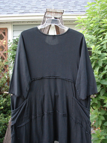 Barclay Reverse Stitch Double Pocket Tunic Dress, a black shirt on a clothes rack. Exterior flutter seams, lettuce-edged sleeves, drop front wrap around pockets. Three-quarter length sleeves, varying hemline. Size 2.