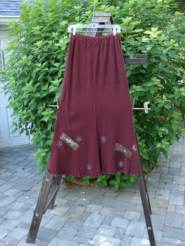 1996 Thermal Swirl Skirt Moon Cayenne Size 2: A red pants and long red skirt on a clothes line and rack, with a wooden object and a close-up of a plant.