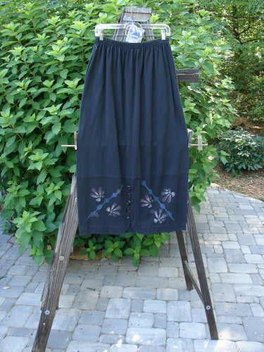 1997 NWT Indra Skirt: A skirt on a rack, featuring a blue skirt with a flower design on it. Perfect condition, made from organic cotton. Full elastic waistline, double paneled lower, colorful chiseled buttons, and abstract floral theme paint. Waist 28-50, hips 50, length 38 inches.