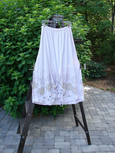 Barclay Spring Shade Skirt, a white skirt with a flower design on it. Made from organic cotton. Features include a full elastic waistband, varying hemline, and extra long rippie cord. Size 2.