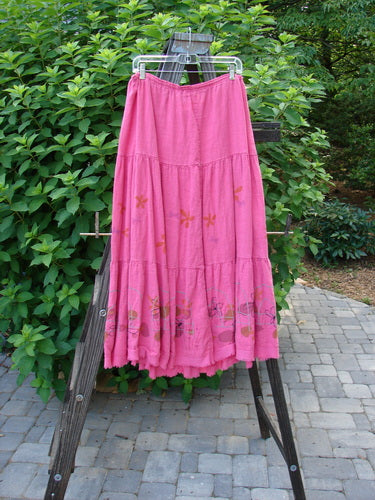 Barclay Linen Drawstring Ruffle Skirt Daisy Fence Flamingo Size 2: A pink skirt with a flower design, featuring a drawstring waistline, alternating horizontal seams, and a billowy flare with sweet fringe edges. Length: 37 inches.