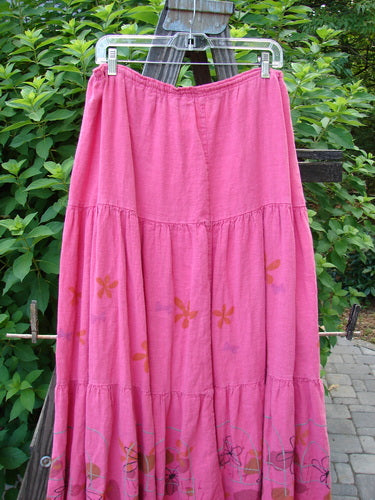 Barclay Linen Drawstring Ruffle Skirt Daisy Fence Flamingo Size 2: A pink skirt with a flower design on a clothes line, featuring a full drawstring waistline, alternating horizontal seams, and a slight billowy flare with sweet fringe edges. Perfect for building a special look with a sweet daisy theme. Length: 37 inches.