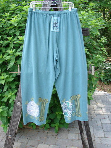 A pair of 1993 Crop Pant Pinwheel Grey Green Size 1 on a wooden stand. Features include an elastic waistline, shorter inseam, and a signature Blue Fish patch.