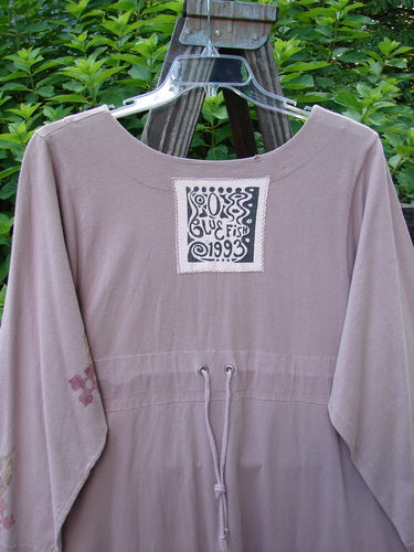 1993 Modernismo Duster Dress Columns Ash Pink OSFA: A purple shirt with a logo patch, wooden buttons, and kangaroo pockets.