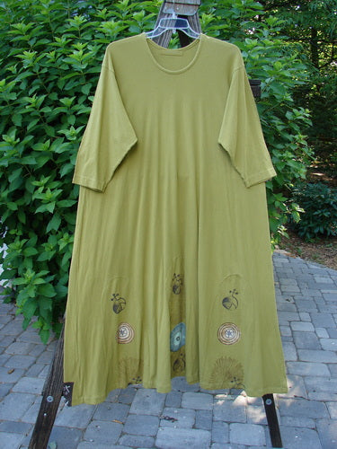 1998 Mystic Dress Celestial Terra Vert Size 2: A green dress with a super bubble hemline, rope cord tie, and abstract pinwheel theme paint. 3/4 length sleeves and a smaller rounded neckline.