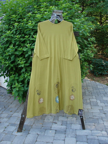 1998 Mystic Dress Celestial Terra Vert Size 2: A green dress on a rack. Super A-line shape with rounded vertical inserts for swinging fullness. 3/4 length sleeves and a rope cord tie. Organic cotton, detailed pinwheel theme paint.