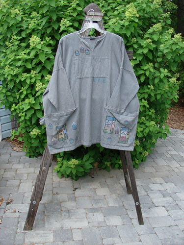 A grey shirt on a wooden rack, featuring a design, oversized pockets, and drop shoulders. Barclay Patched Canvas Urban Tunic Top Village Grey Stone Size 2.