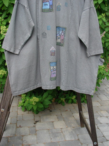 Image alt text: "Barclay Patched Canvas Urban Tunic Top Village Grey Stone Size 2 - Grey shirt with drawing, button, wooden leg, plant, and stone floor details"