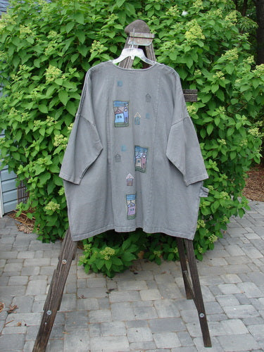 A grey Barclay Patched Canvas Urban Tunic Top with a picture on it. Features include split front rolled neckline, oversized pockets, drop shoulders, and village theme paint. Made from heavy weight hemp twill. Size 2.