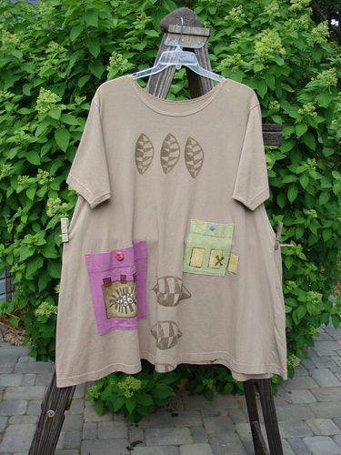 Image: A brown shirt with patches on it, featuring a green patch with a blue button. 

Alt text: 1997 Montage Dress Triple Leaf Wheat Size 2: A brown shirt with colorful patches, including a green patch with a blue button.
