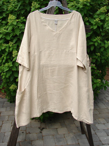 A white Barclay Linen Urchin Side Pocket Tunic Dress, size 2, on a clothes rack. Three-quarter length sleeves, V-shaped neckline, empire waist seam, and varying hemline.