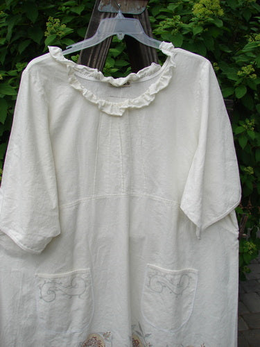 Image alt text: Barclay Linen Duet Sunrise Dress, a white shirt on a swinger, with a plastic swinger on a wood surface.